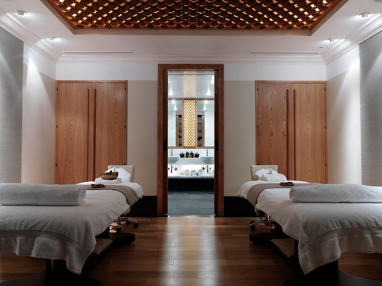 Spa treatment room with wooden lattice ceiling, two beds and wooden wardrobes and floors
