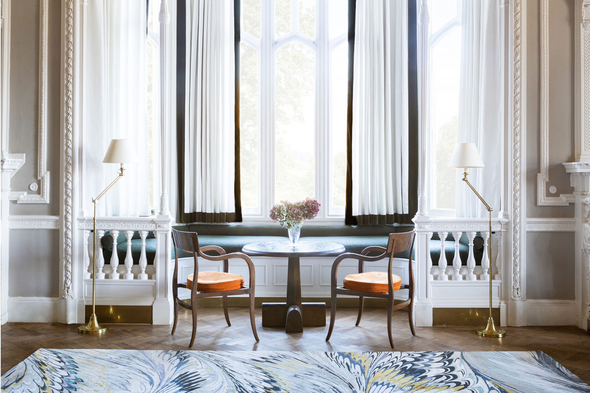 A view of a grand window featuring a marbled rug from The Rug Company with two chairs in orange cushions