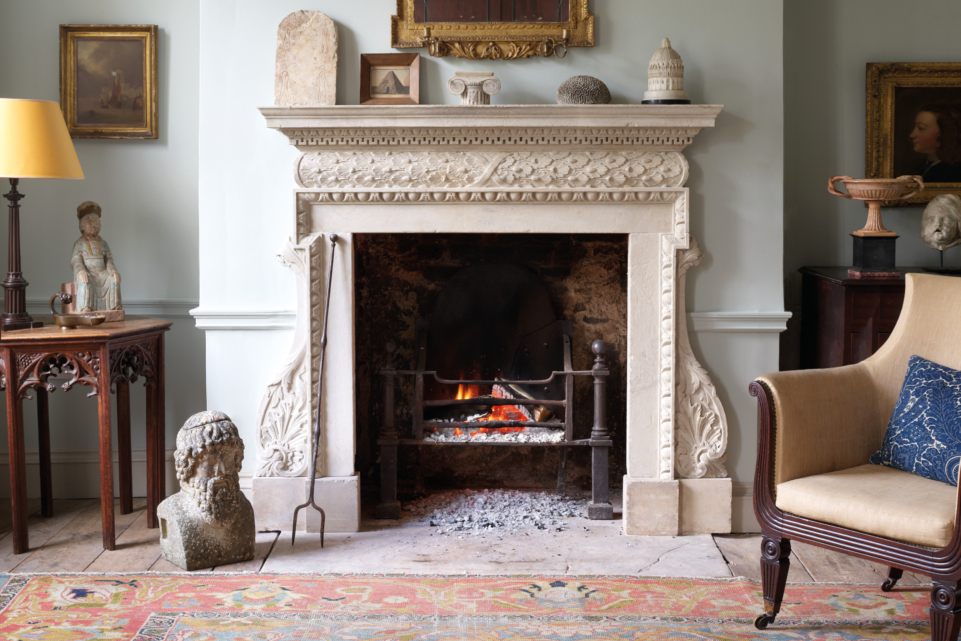 Close up of a traditional fireplace, with a rug, armchair and sculptures in the foreground