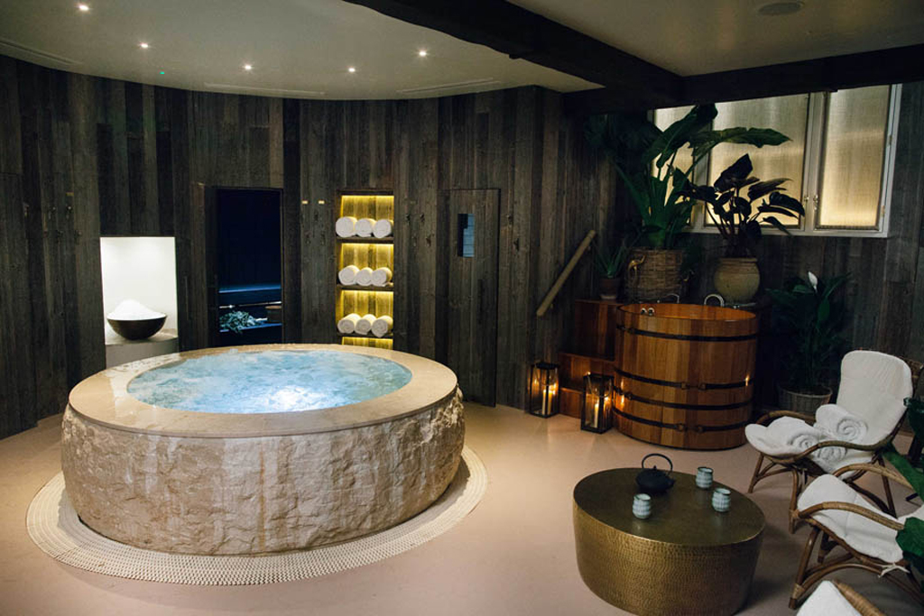 Wooden panelled room with stone jacuzzi tub and towel-strewn chairs