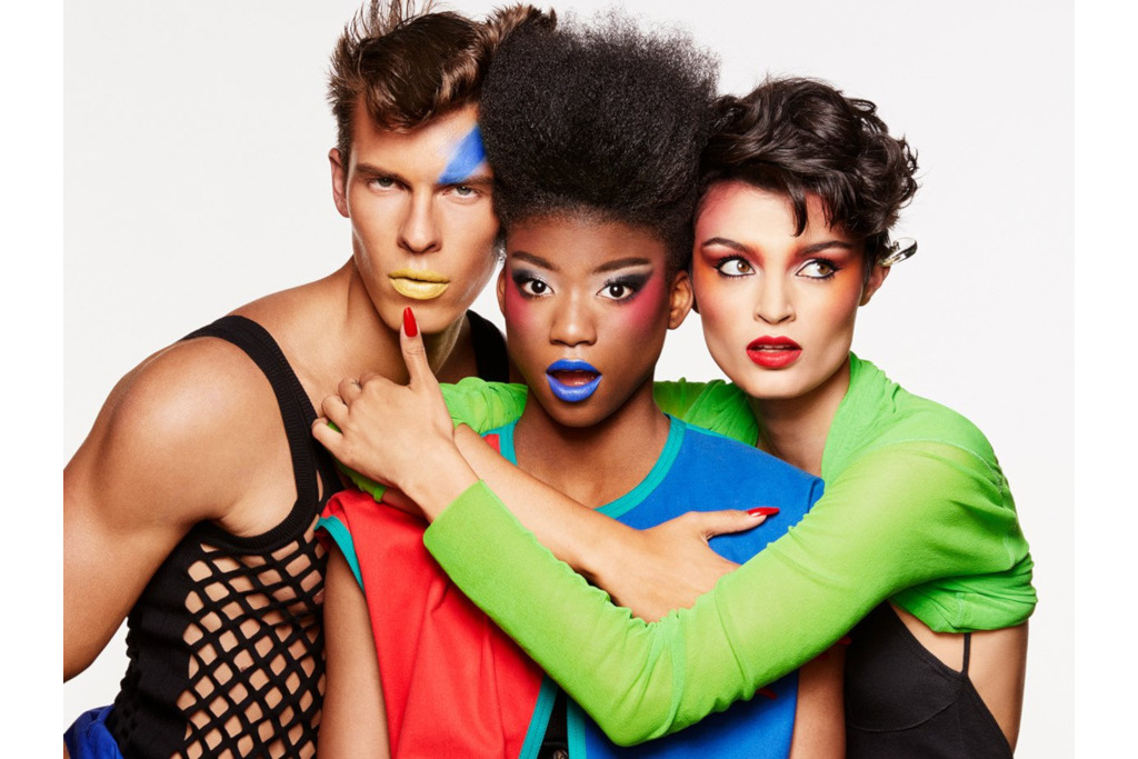 Three models stood close together in colourful clothing and glam rock makeup