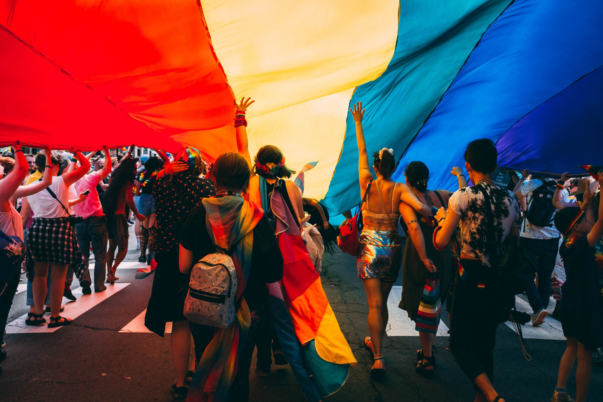 People walking in a pride parade under a rainbow flag