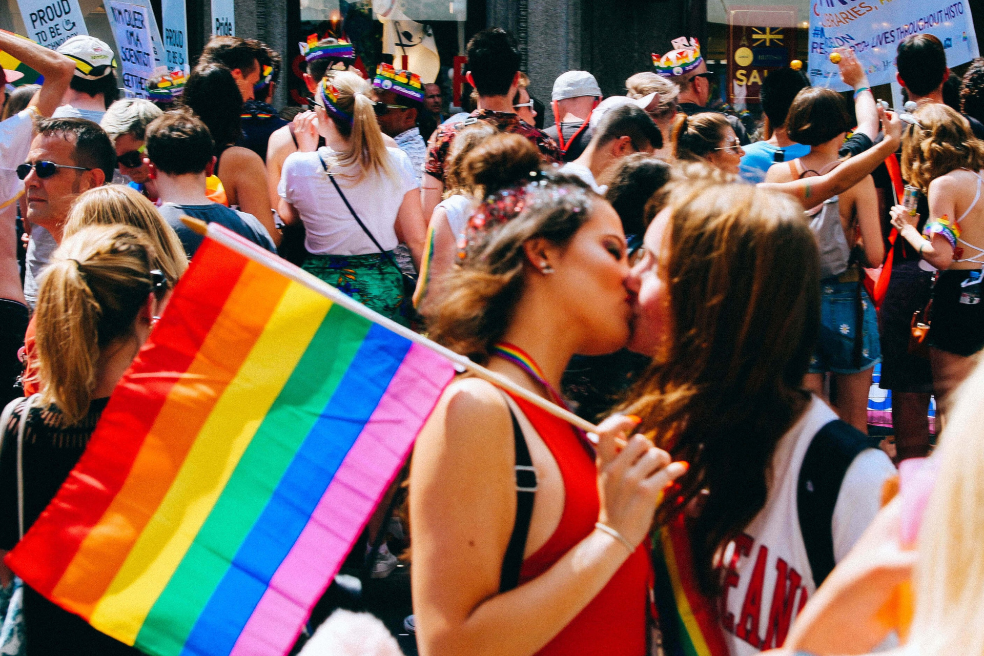 Two women kissing holding a pride flag amongst a crowd of people