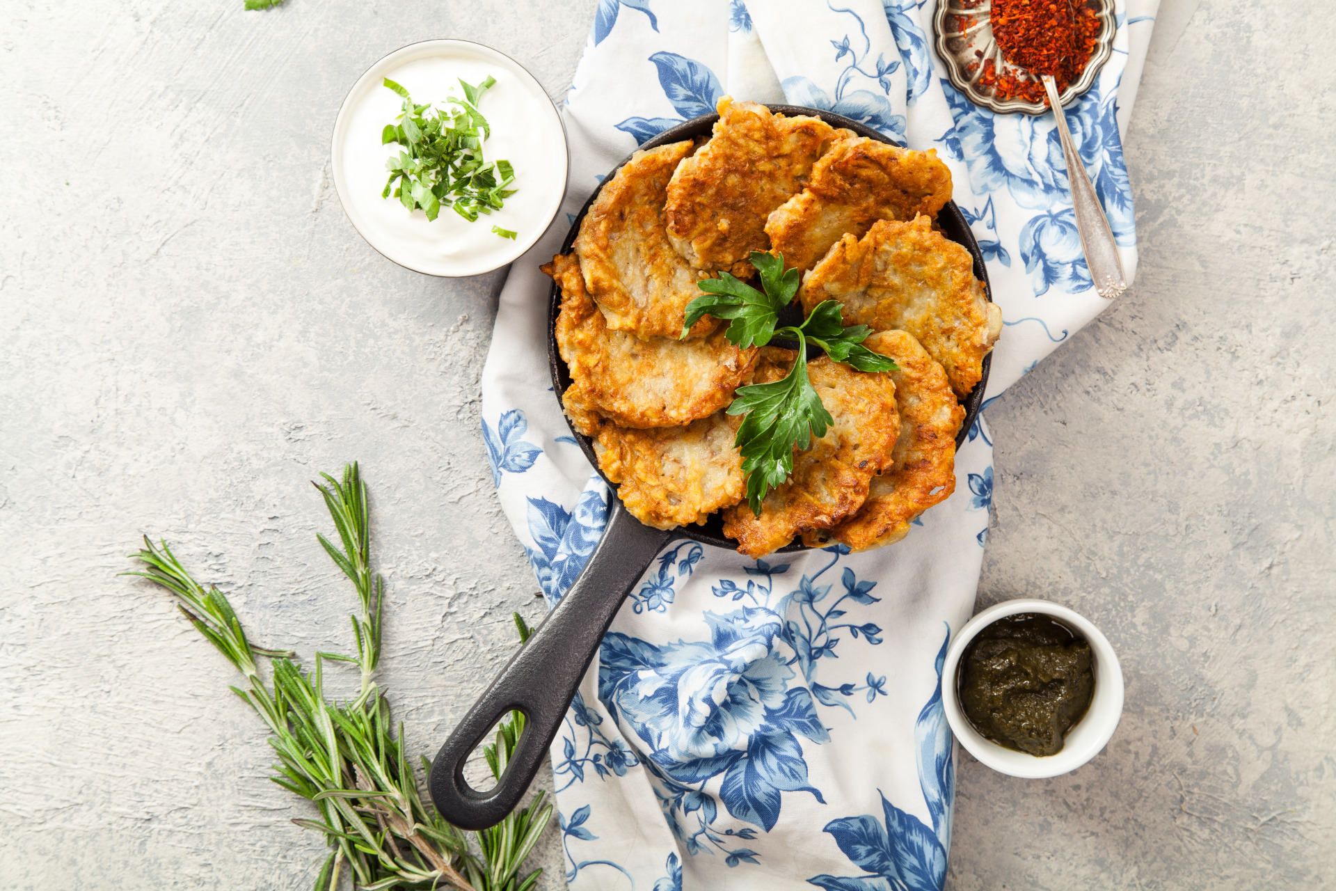 Potato latkes traditional jewish pancakes with sour cream, parsley, dry red pepper flakes and mint sauce. Background, white napkin with blue flowers