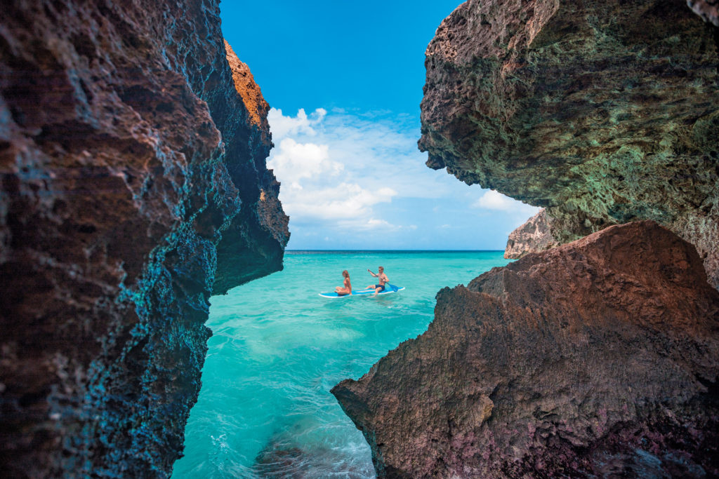 Two people paddleboarding in the Caribbean sea, at a hidden gem between the rocks