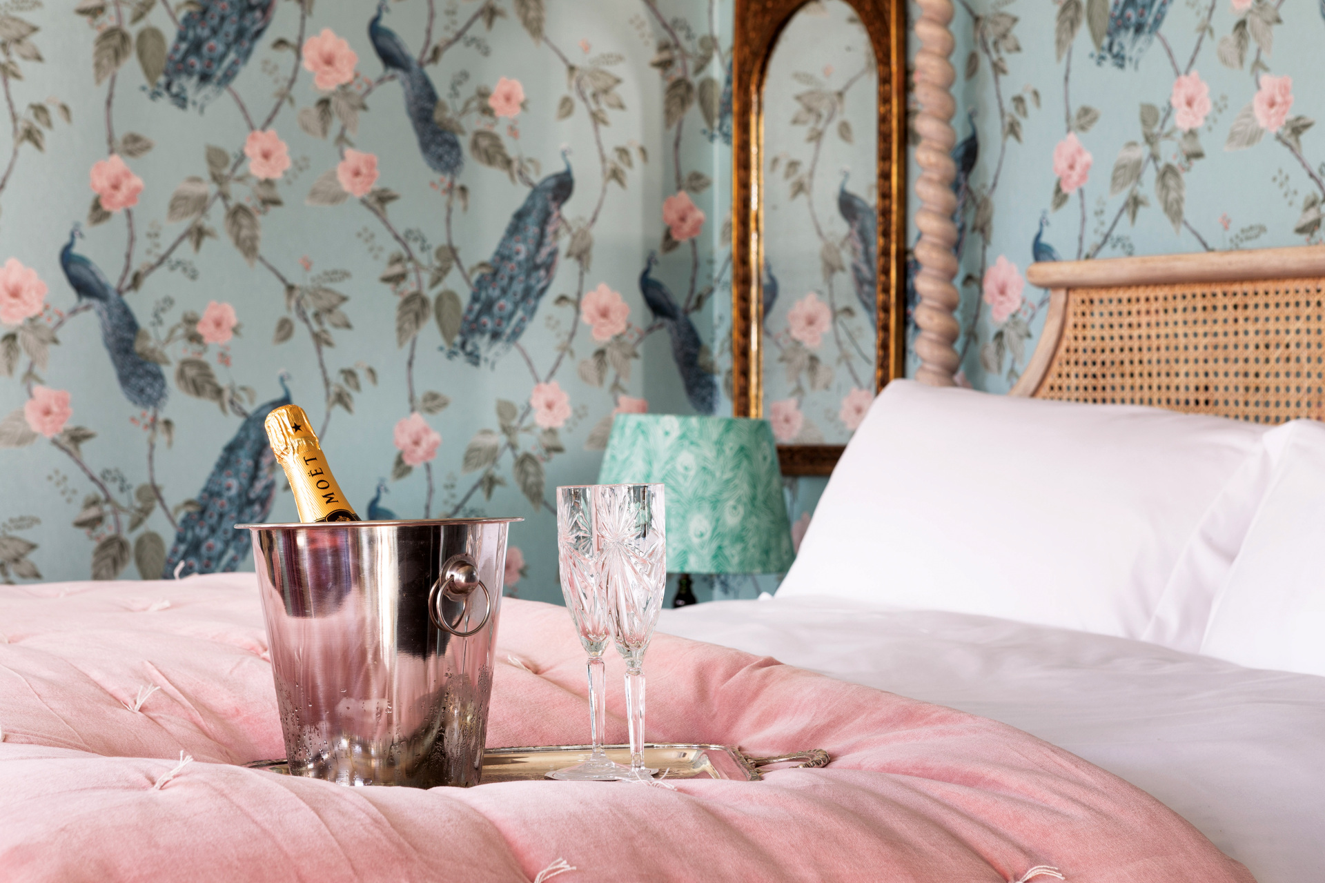Bed with pink bedspread, a bottle of champagne and glasses on top