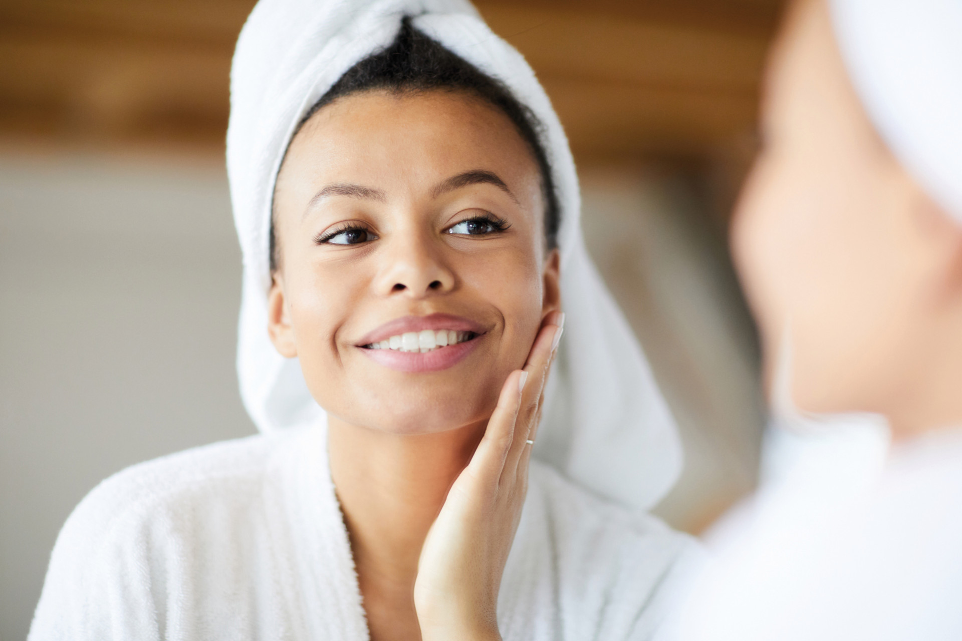 Head and shoulders portrait of smiling Mixed-Race woman looking in mirror during morning routine, copy space