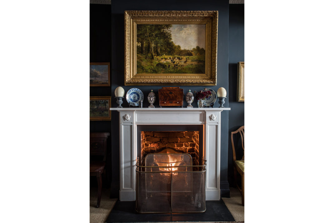 White fireplace with navy painted walls and oil painting hung above