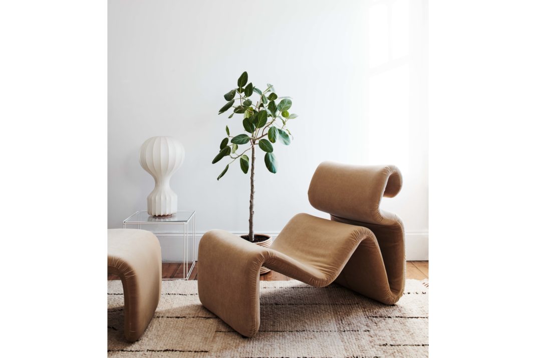 Modernist sitting area with modern camel chair and footstool, plant, neutral rug and white ornament.