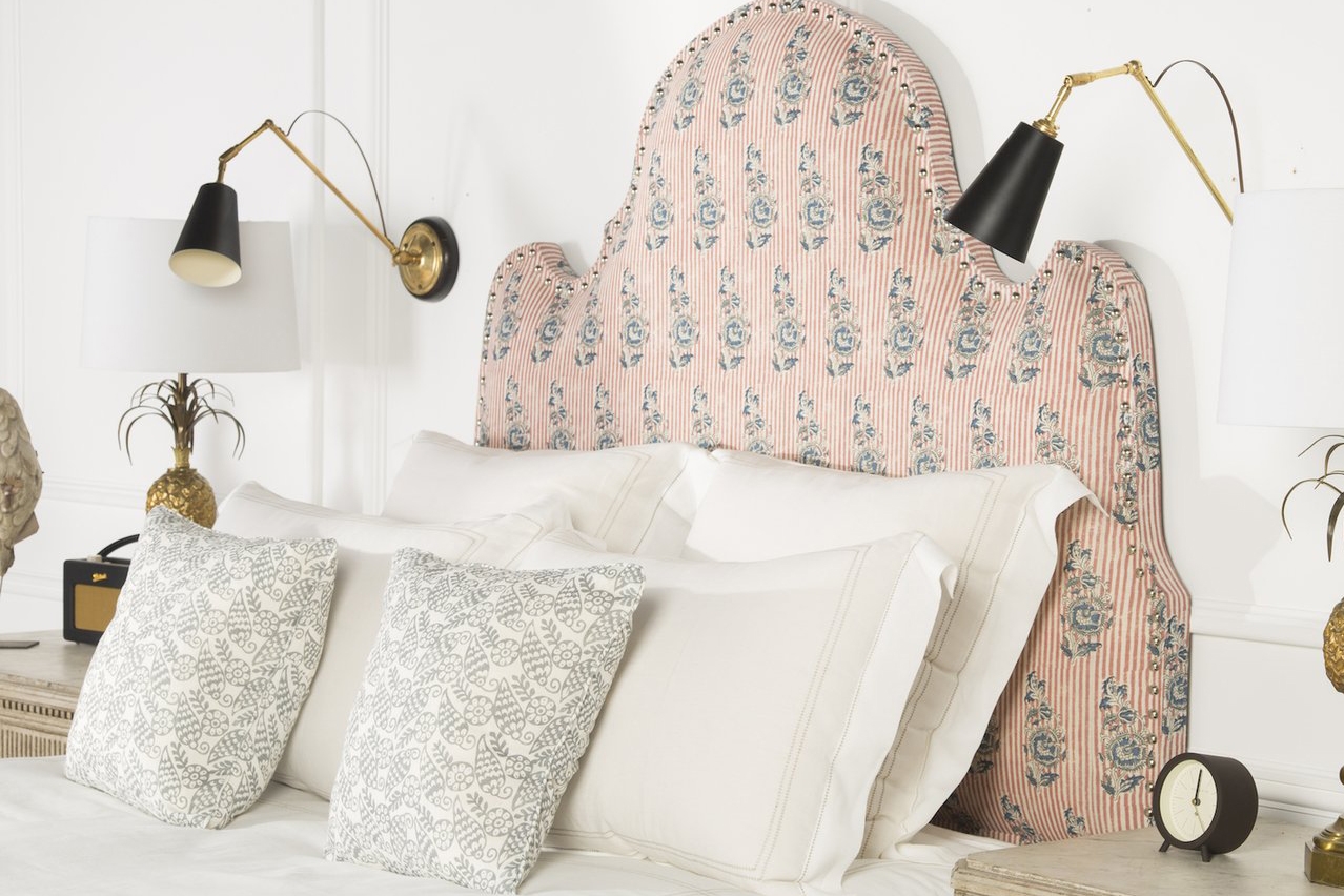 Washed-out pink bedstead, white walls, neutral bedding, black and brass wall lamps