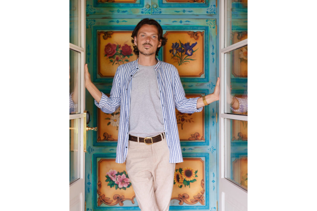 Matthew Williamson standing in doorway. Turquoise and orange patterned wall behind.