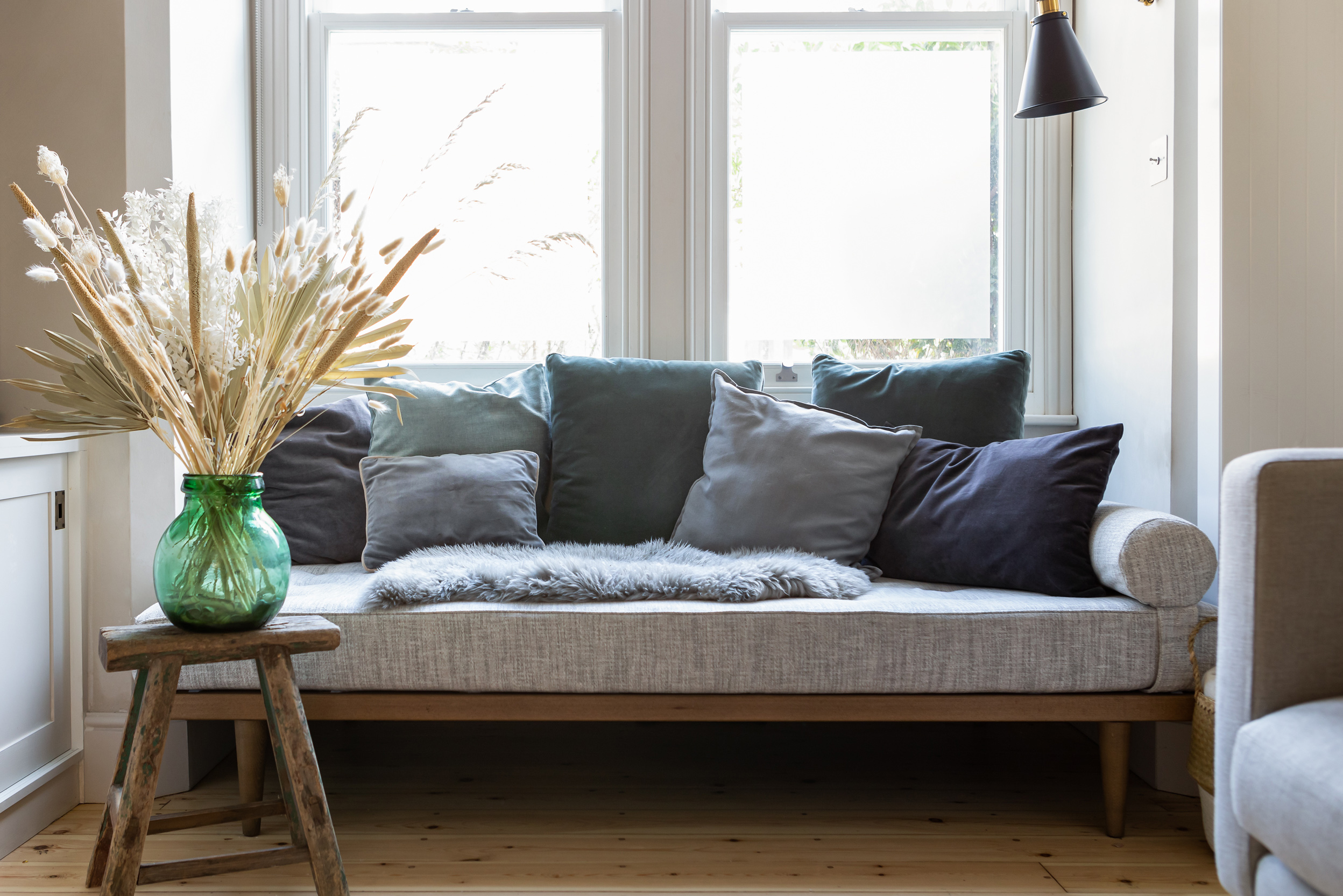 Grey sofa in front of window. Green vase on side table.