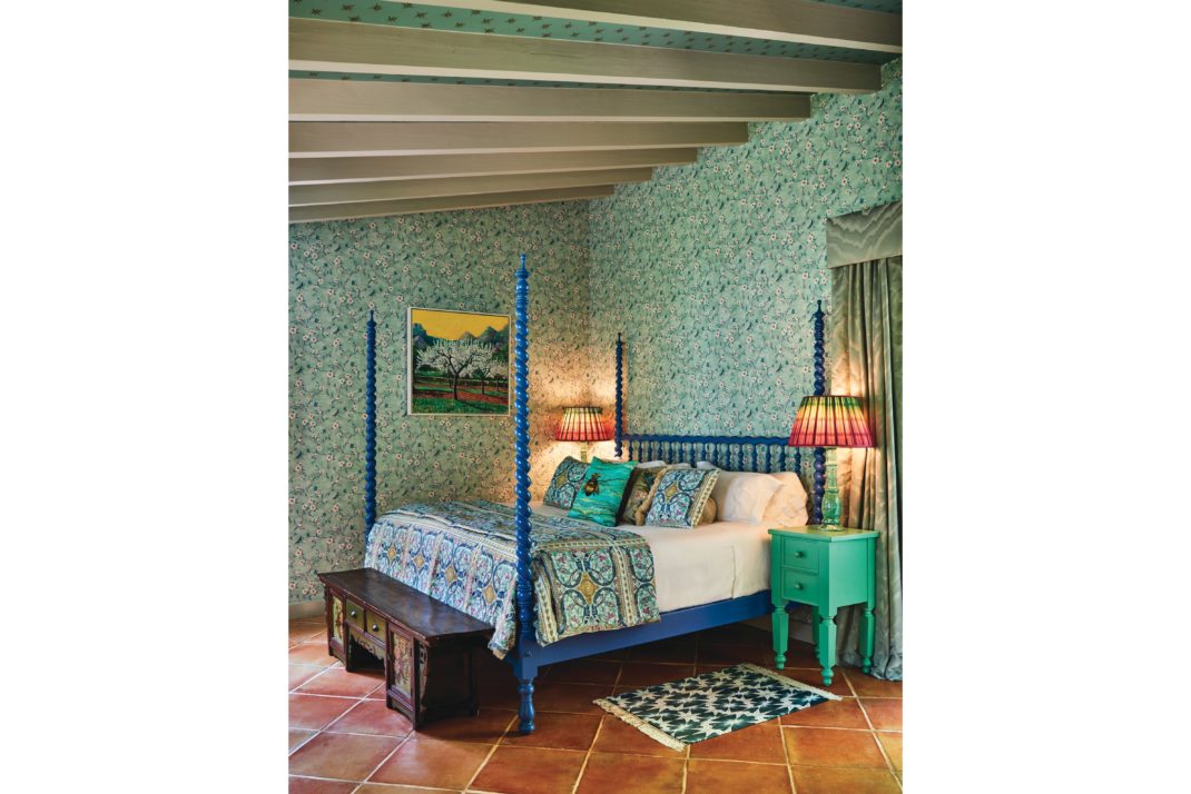 Colourful patterned green room in La Residencia, Mallorca. Blue bed frame, terracotta floors, green side table.