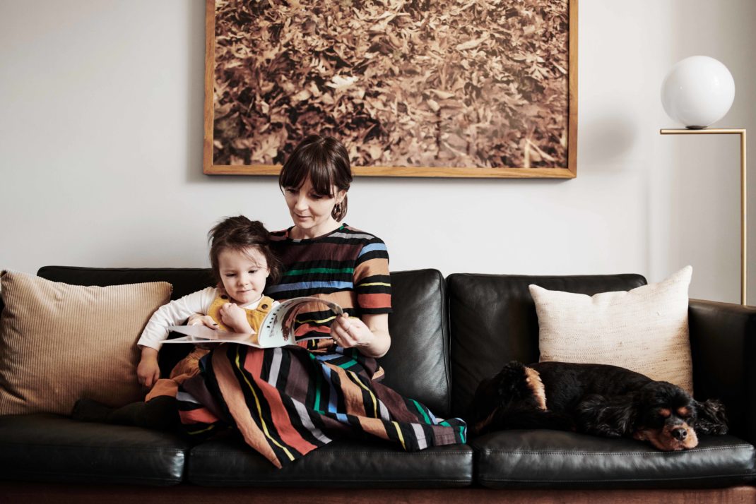 Sheena Murphy and daughter on black leather sofa. In the background: photographic print, modern lamp.