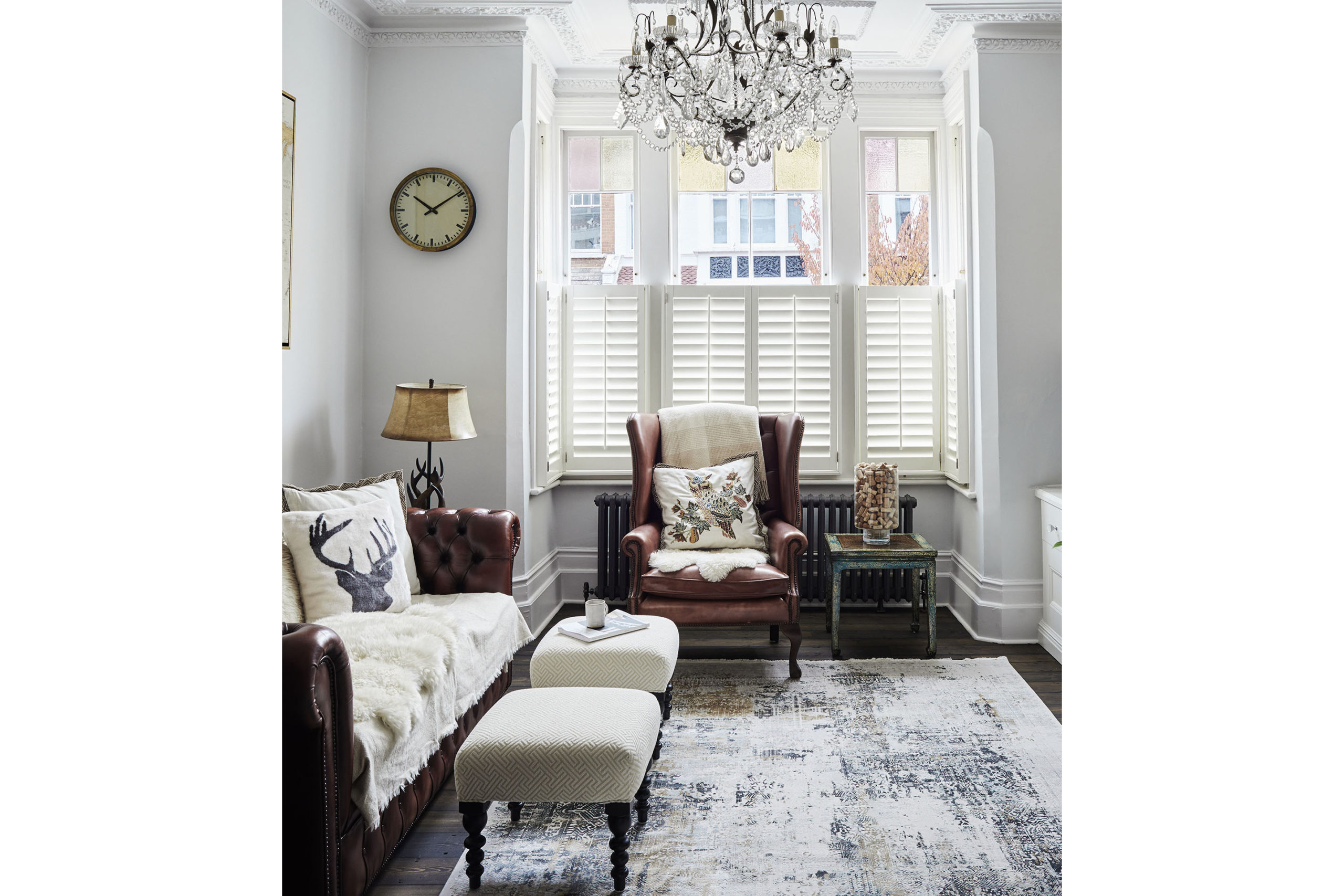 Neutral sitting room with leather chair and sofa. White footstools and rug.