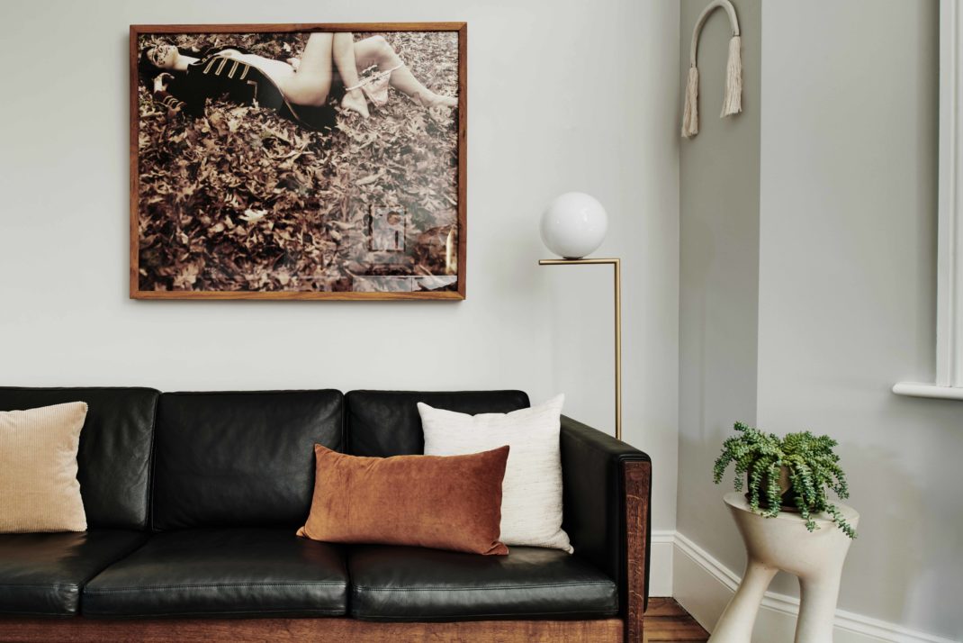 Black leather sofa with neutral and amber cushions. In the background: Sepia photograph of woman.