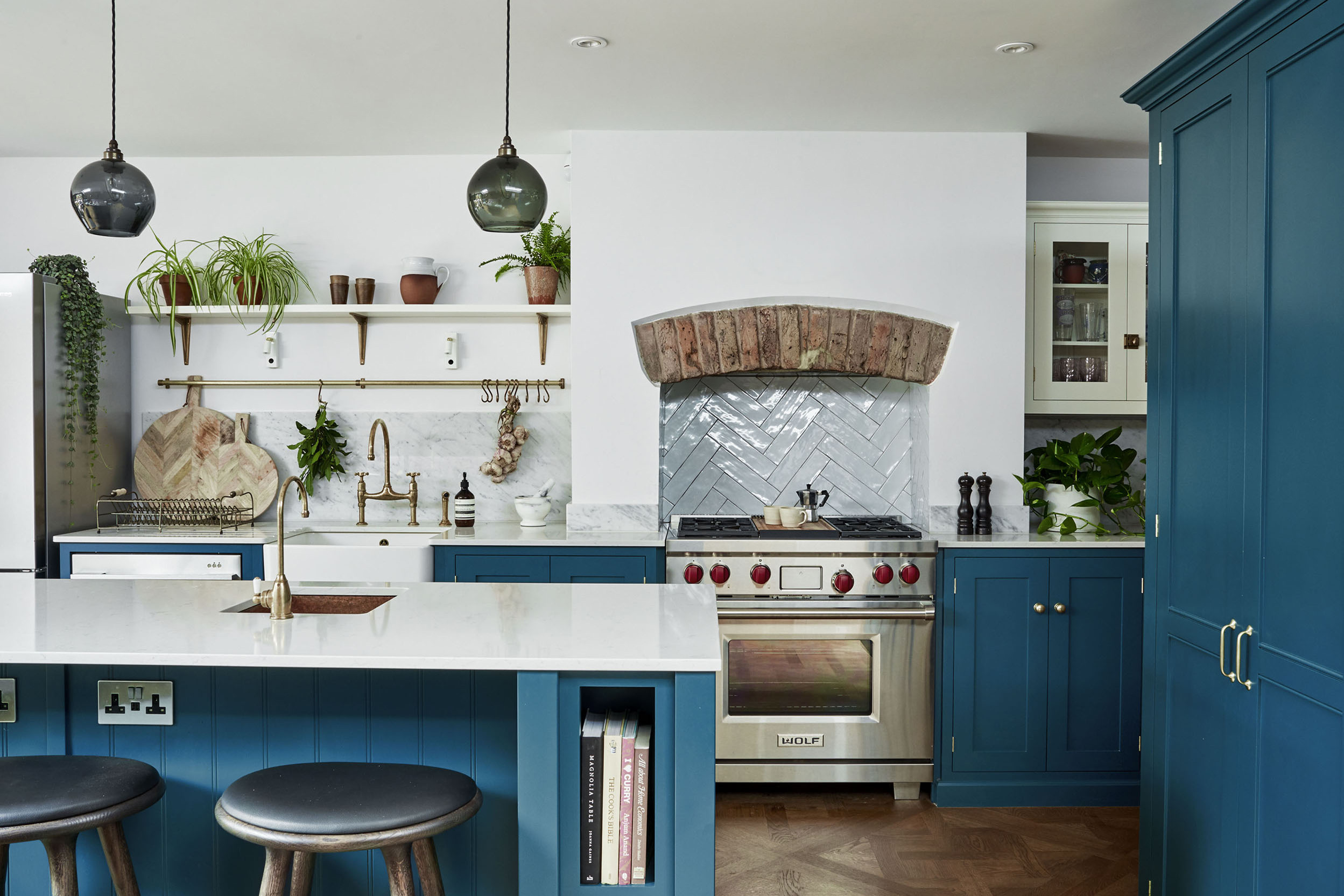 Teal kitchen with white wall. Hanging pendant lights, kitchen island with stools.