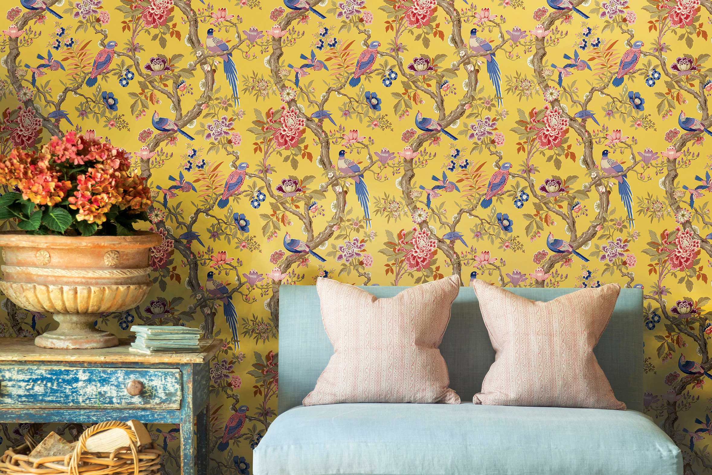 GP & J Baker eltham bird wallpaper - yellow background with colourful birds behind pretty pastel cushioned chair and bedside table