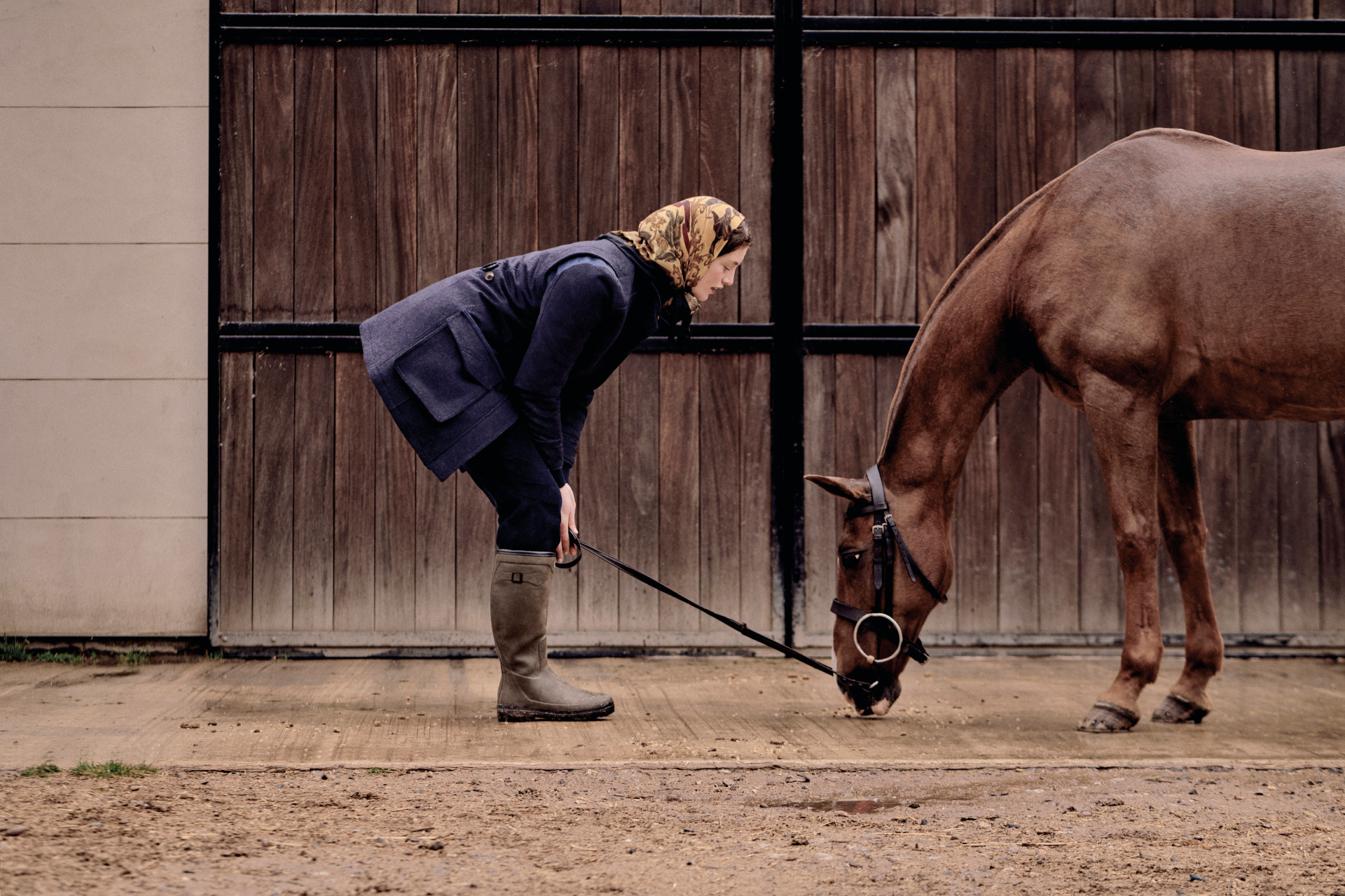 Woman crousching down in front of horse by stables