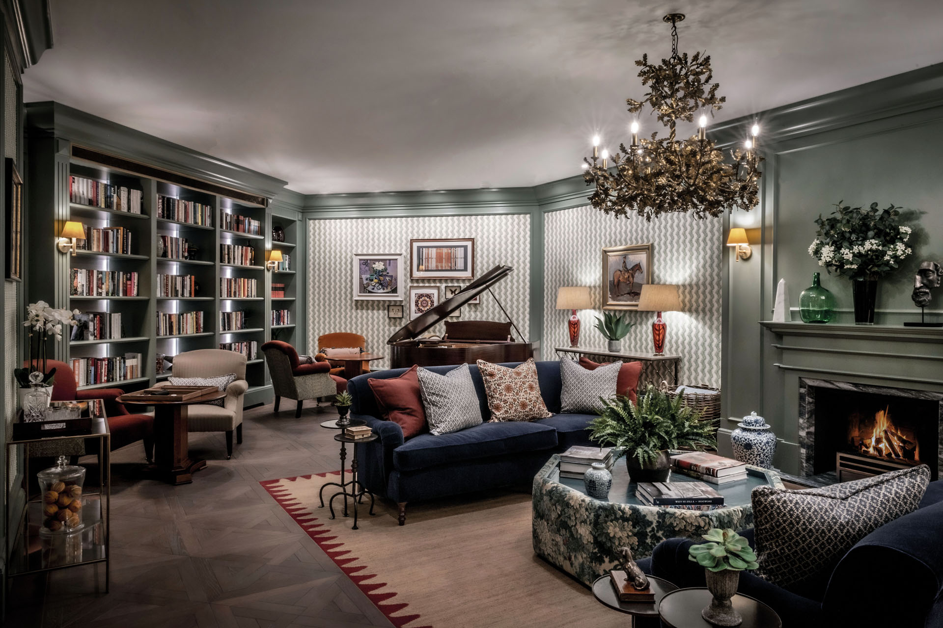 christmassy shot of living room withsofa, grand piano, bookshelves and chandalier with leafy decor - featuring george smith interior
