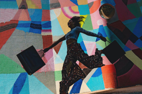 Woman holding bags in front of colourful wall by Harry Cunningham | second hand September