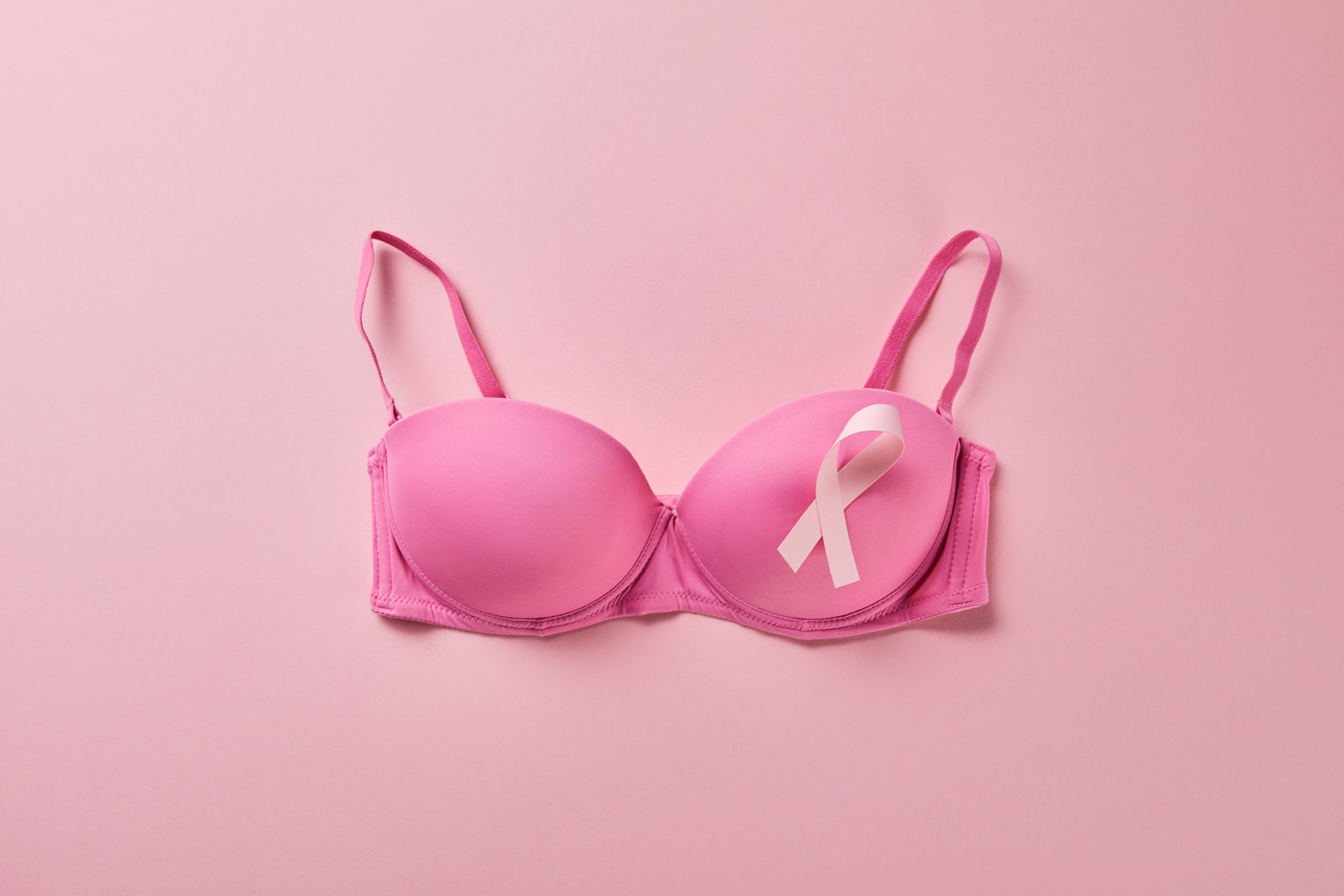 Time to Unite - top view of ribbon on brassiere on pink background, breast cancer concept