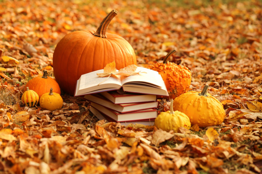 Halloween Horror Novels - Halloween books. Stack of books and orange pumpkins set on autumn foliage on nature background
