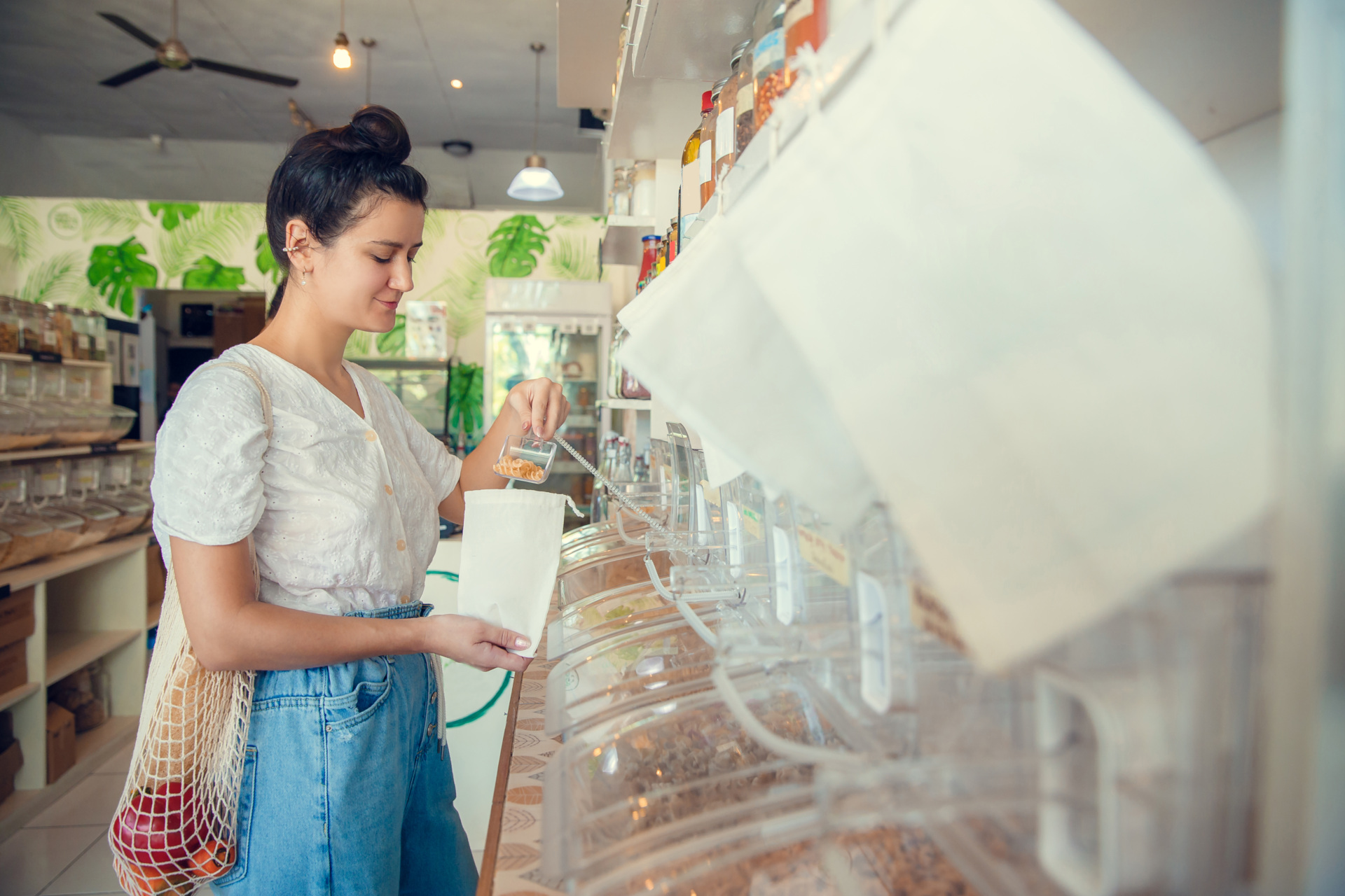 Young woman filling up reusable bag with pasta, nuts or grains in zero waste plastic free store. Low waste lifestyle. Sustainable eco lifestyle