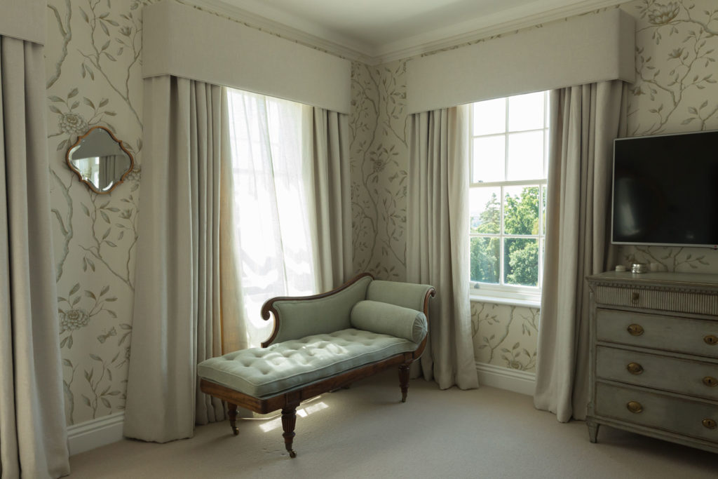 a bedroom with a chaise lounge and grey wallpaper