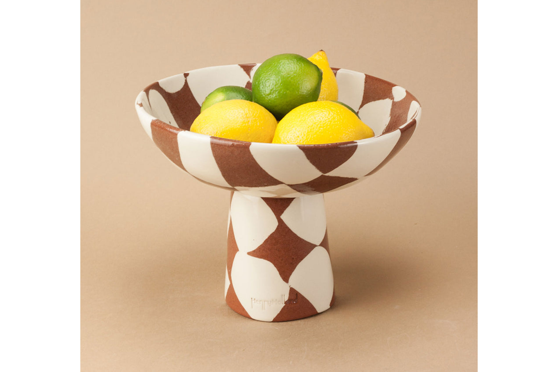 a henry holland fruit bowl with a terracotta and white chequered pattern with three lemons and a lime inside