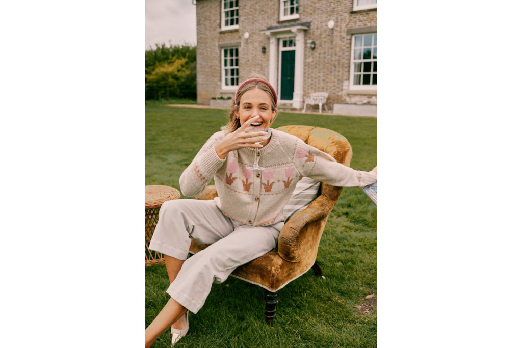 Woman sat on an armchair outdoors wearing a knit cardigan and holding a glass of champagne