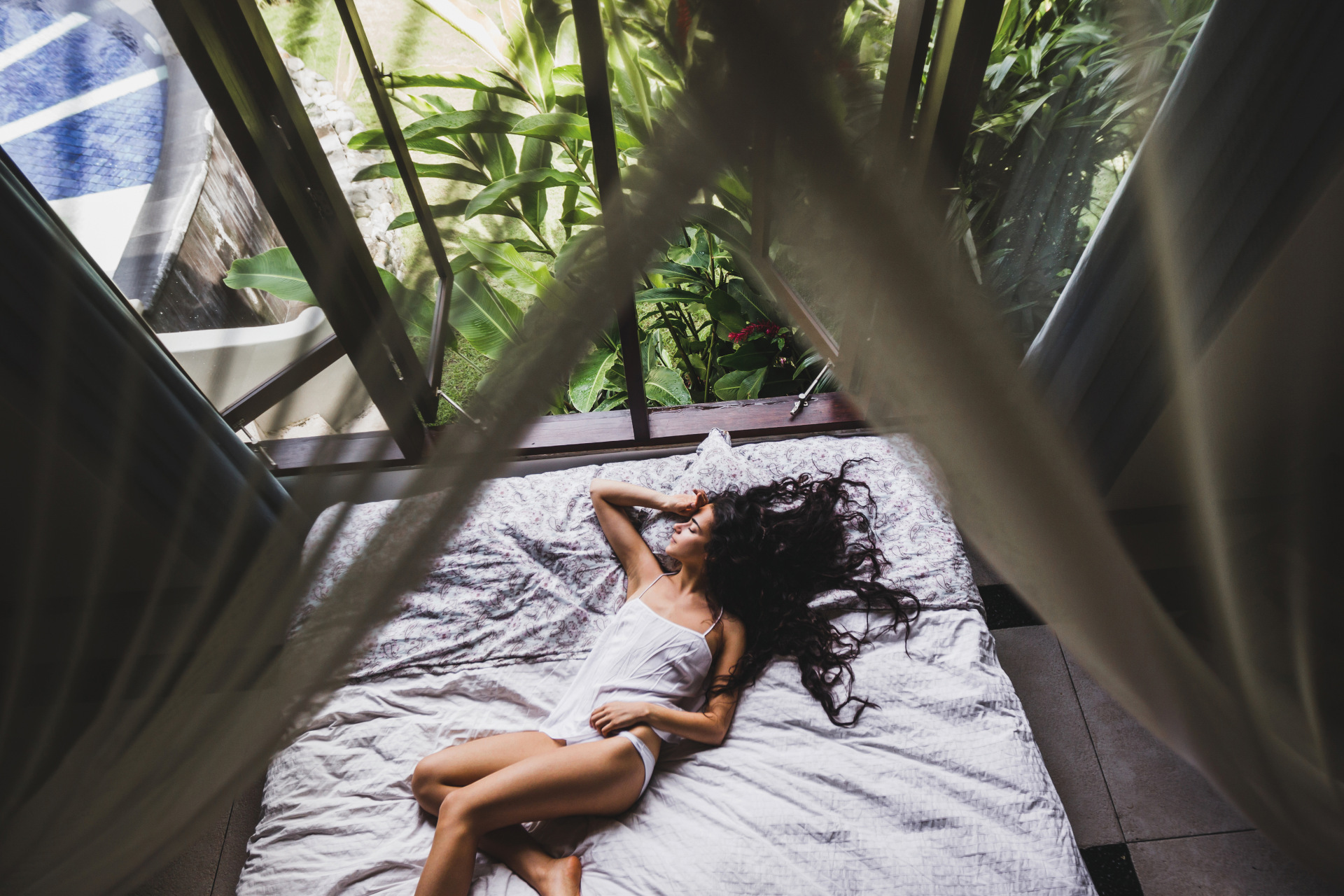 woman sleeping on bed with leafy window behind