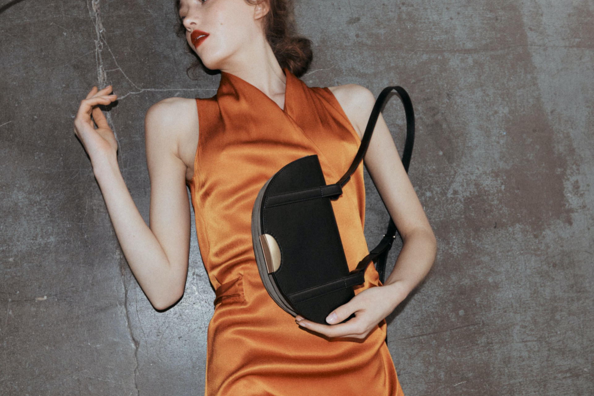 Woman in orange dress laying on floor with black handbag in her arms