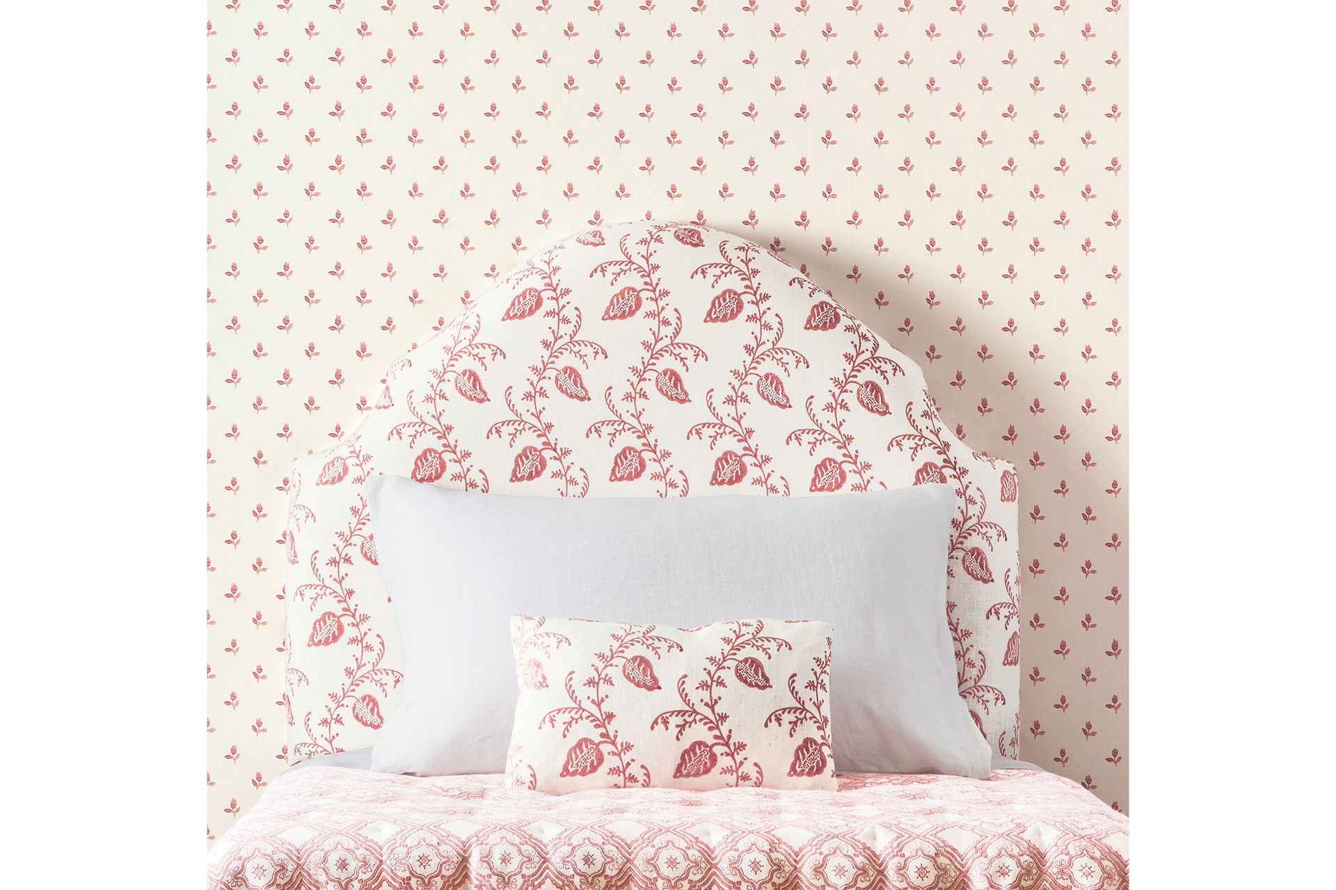 A pink patterned headboard and pink bed lies behind a pink patterned wallpaper byColefax & Fowler