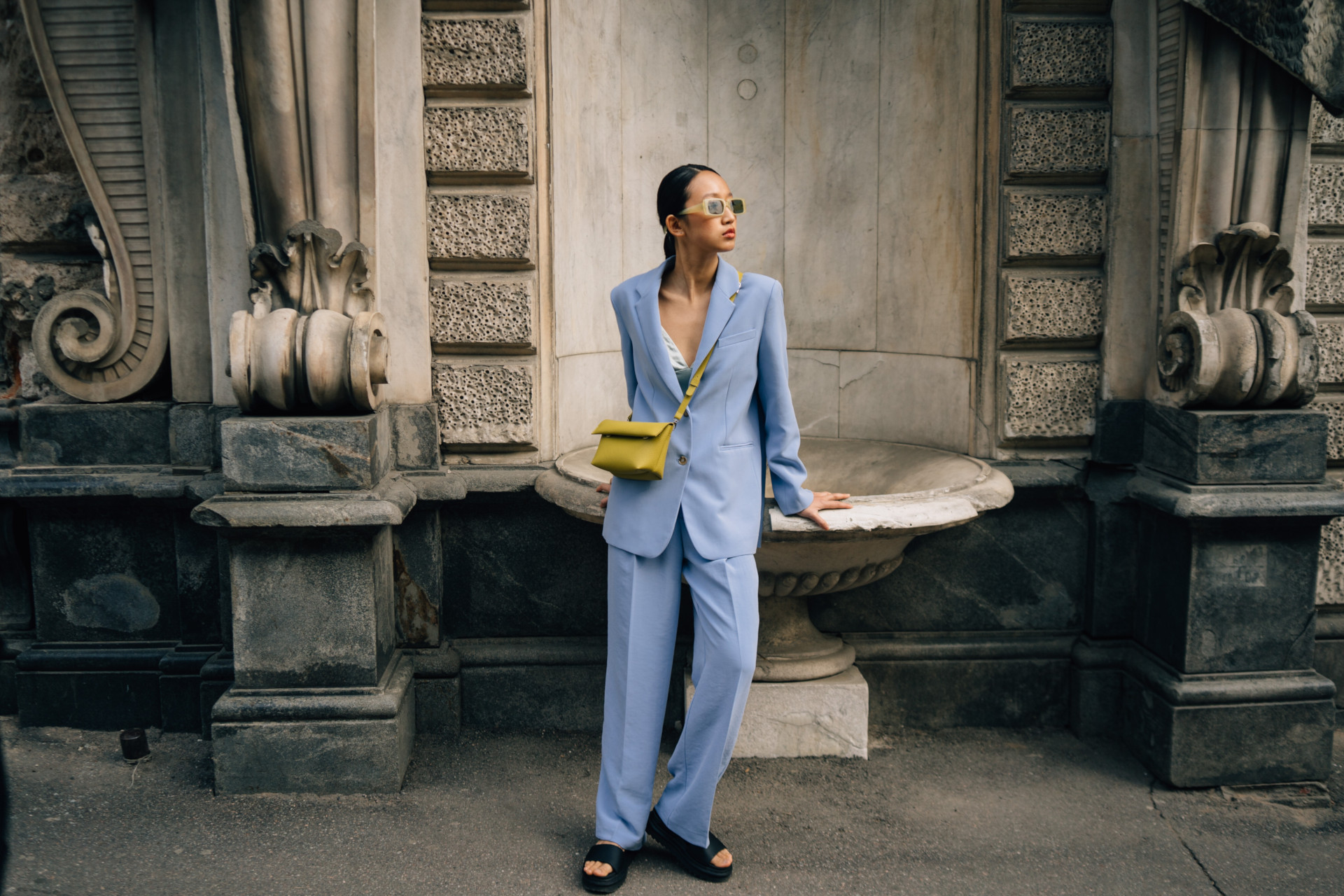 Woman in Blue Suit and Green Handbag Standing Beside Building