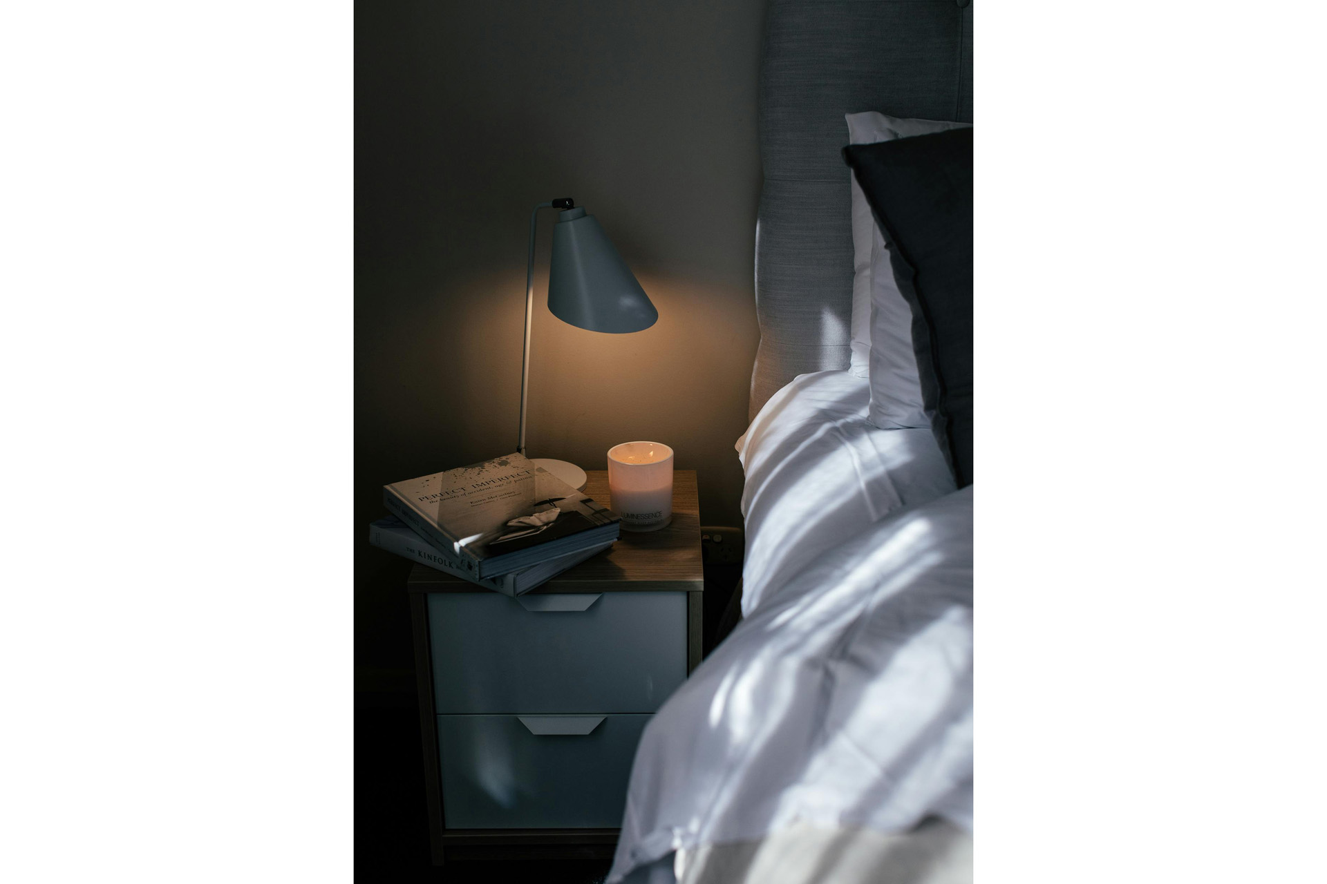 A bed with books and a lamp on the side table