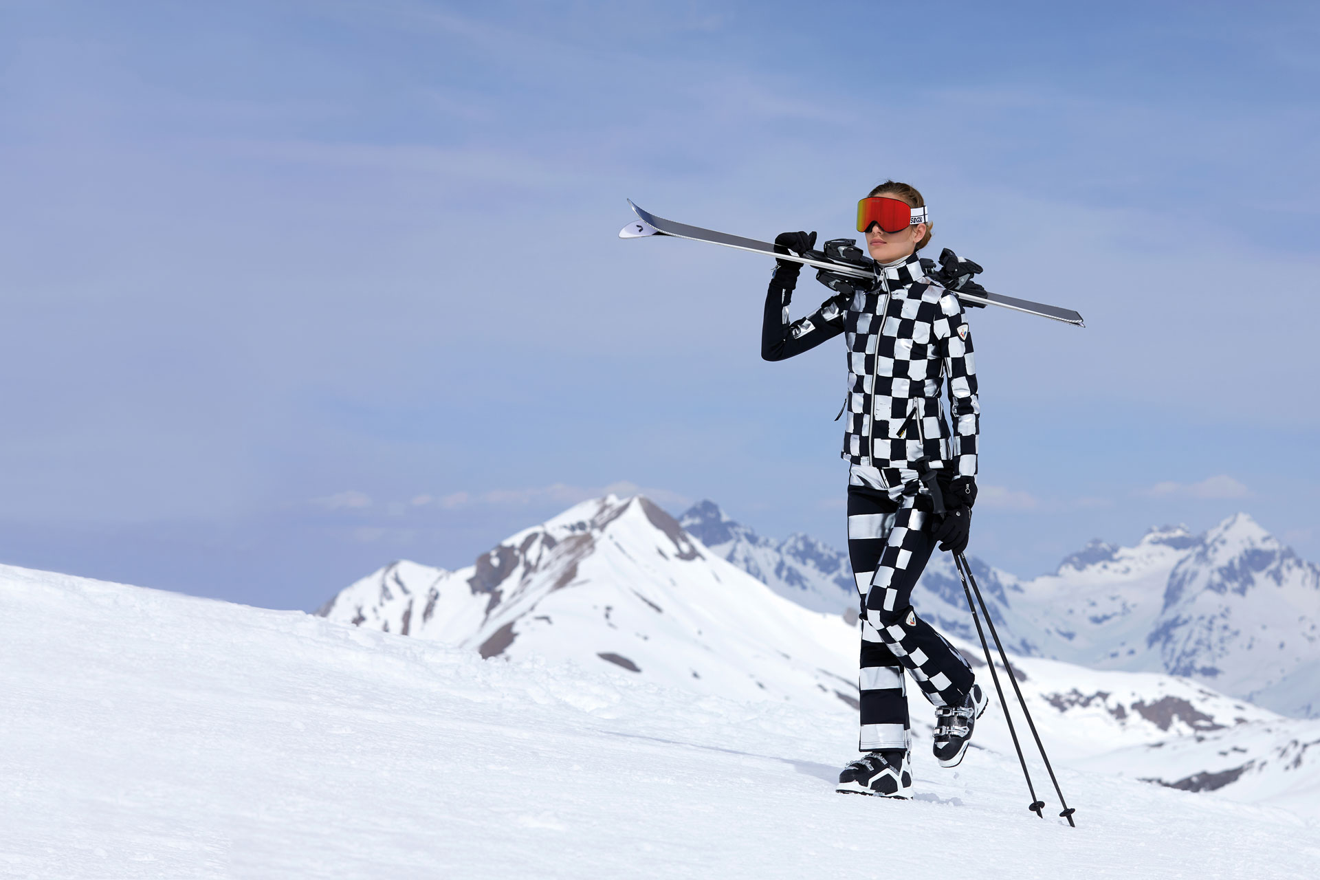 a woman in a chequered ski outfit climbs a snowy slope