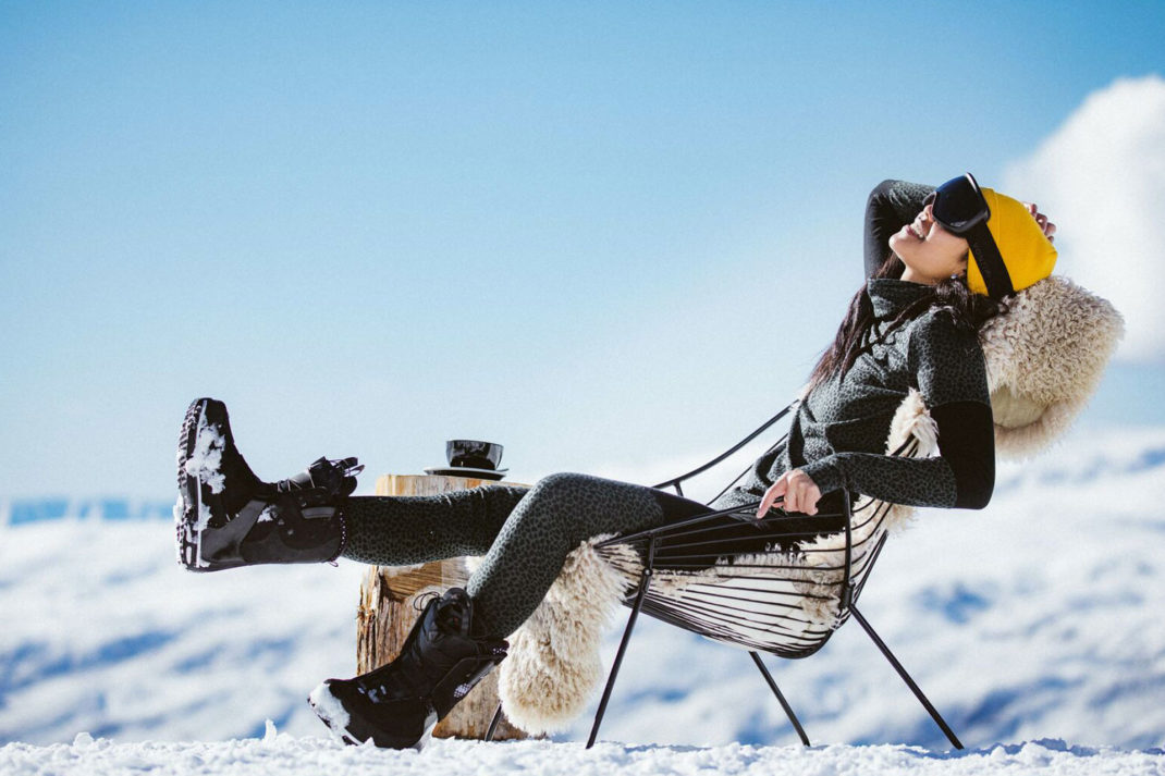 A woman wearing black ski clothing sits on a fur-lined chair on the snowy slopes