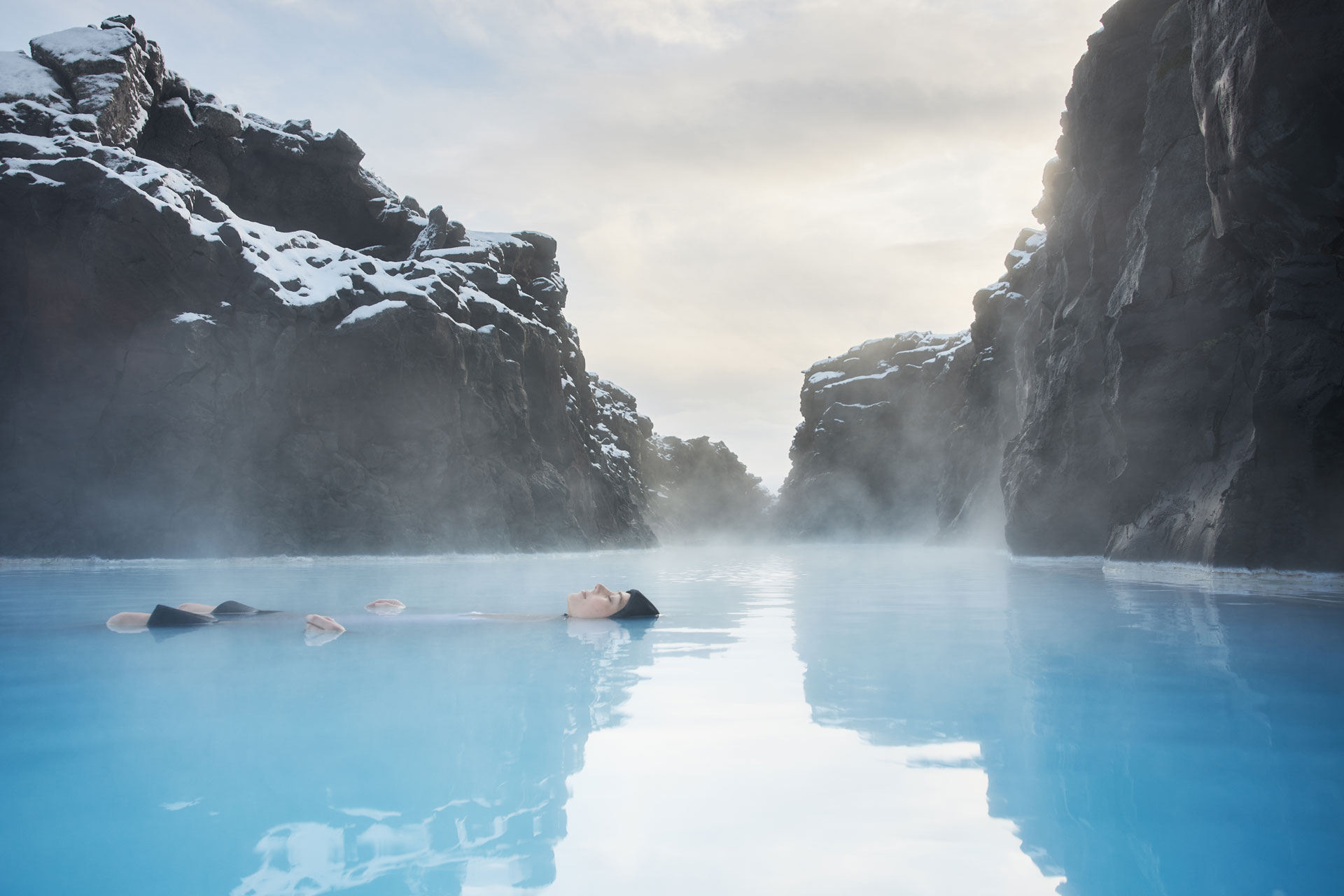 A woman floating on a steamy pool beside snowy mountains