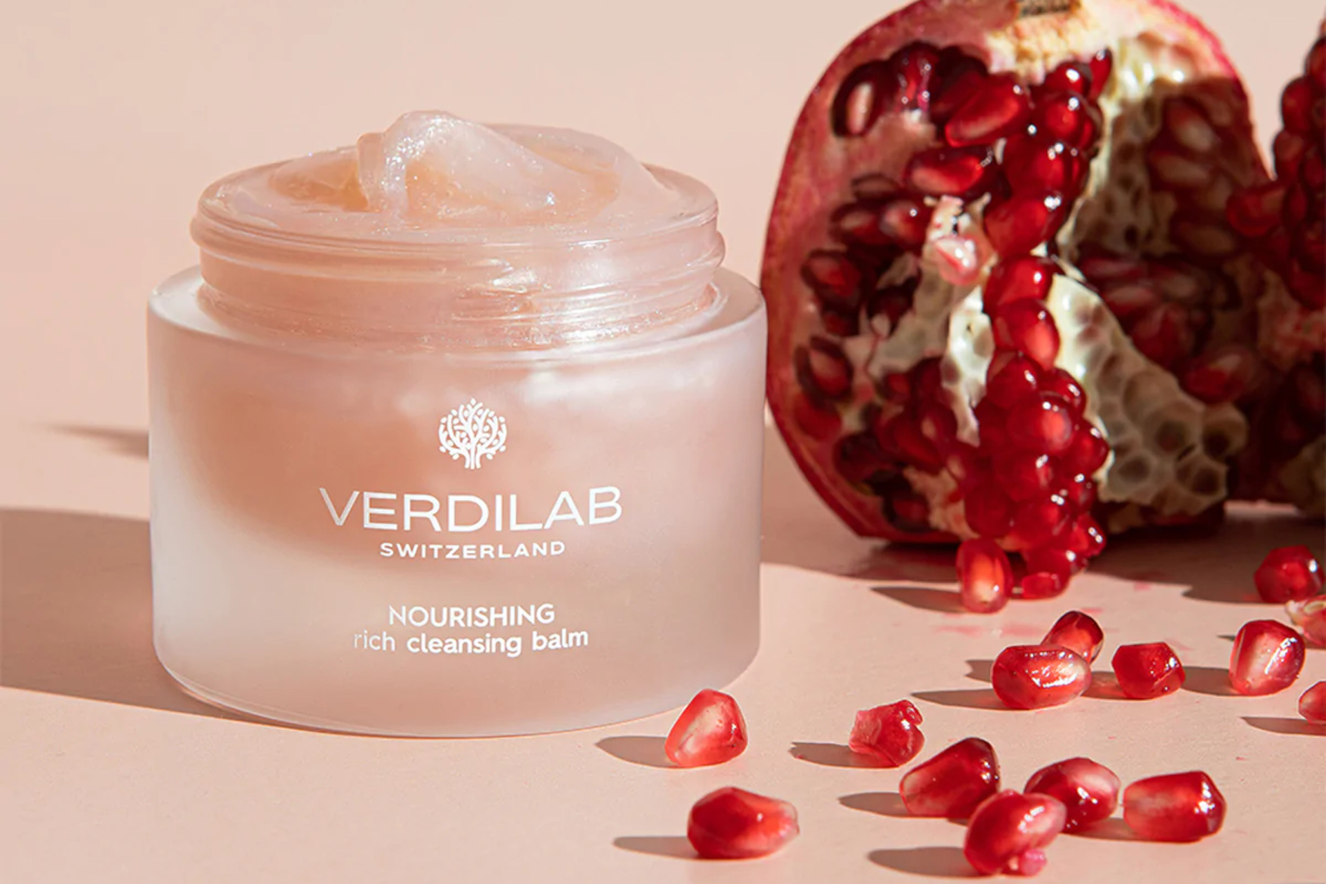 Pink tub of cleansing cream next to pomegranate and seeds