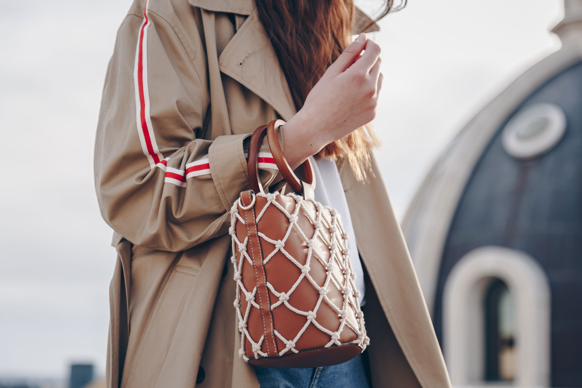 street style fashion details. an attractive woman wearing a beige trench  coat and 90s pattern vintage shoulder mini bag, crossing the street.  fashion outfit perfect for autumn Stock Photo