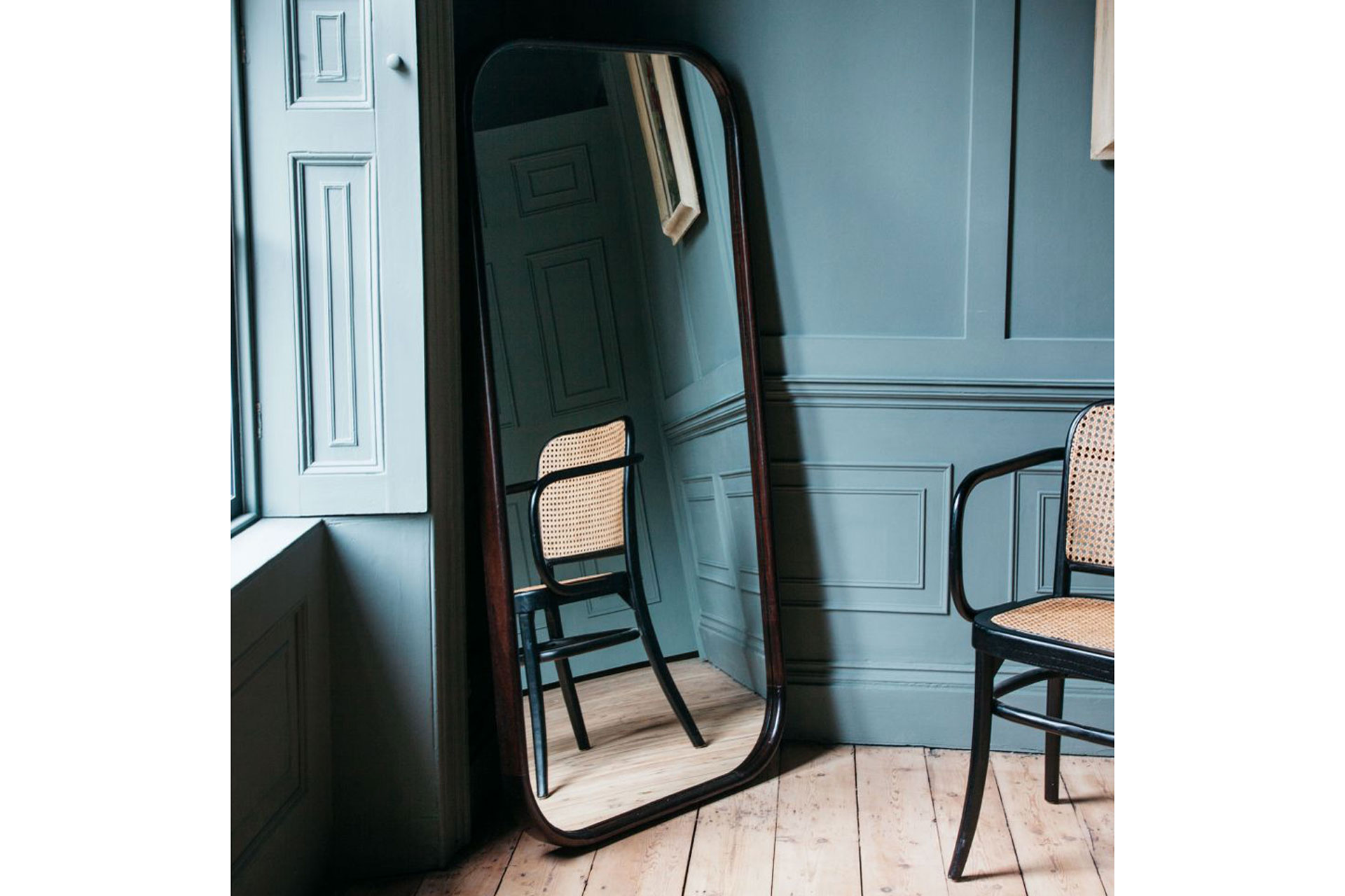 A mirror stands on a blue antique light room with a rattan chair
