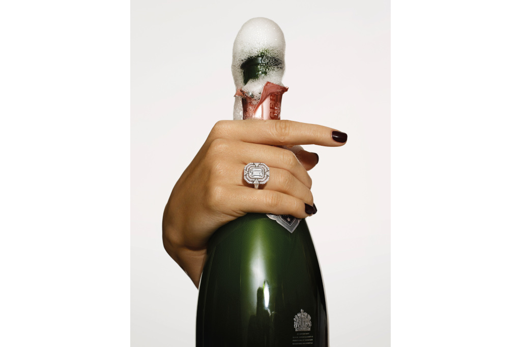 Hand with diamond ring holding champagne bottle