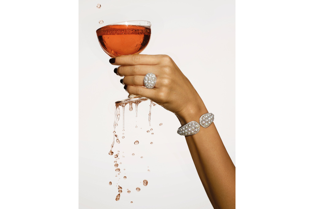 Hand with diamond bracelet and ring holding tipping glass of drink