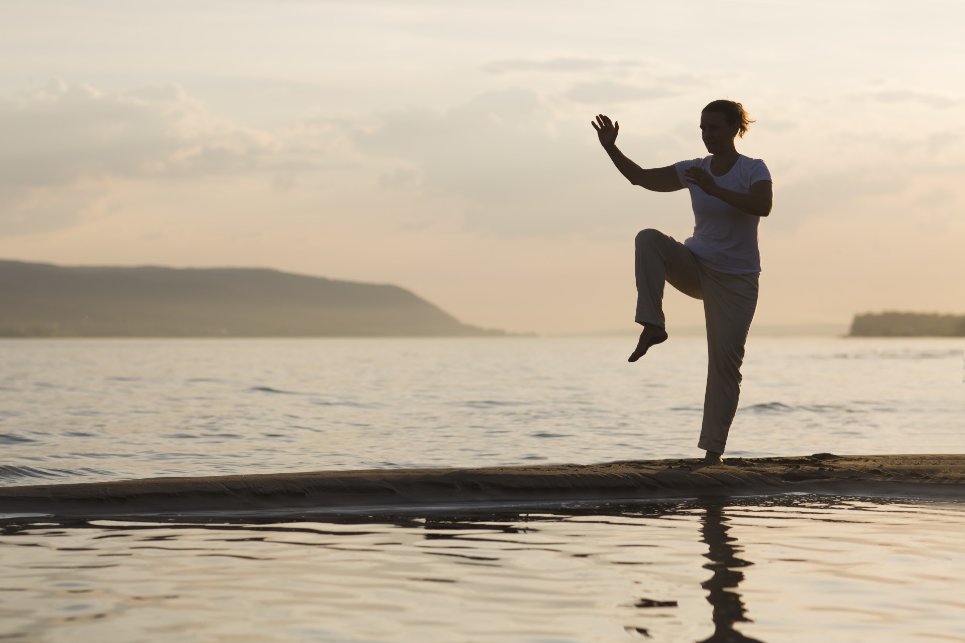 Woman praticing tai chi chuan at sunset on the beach