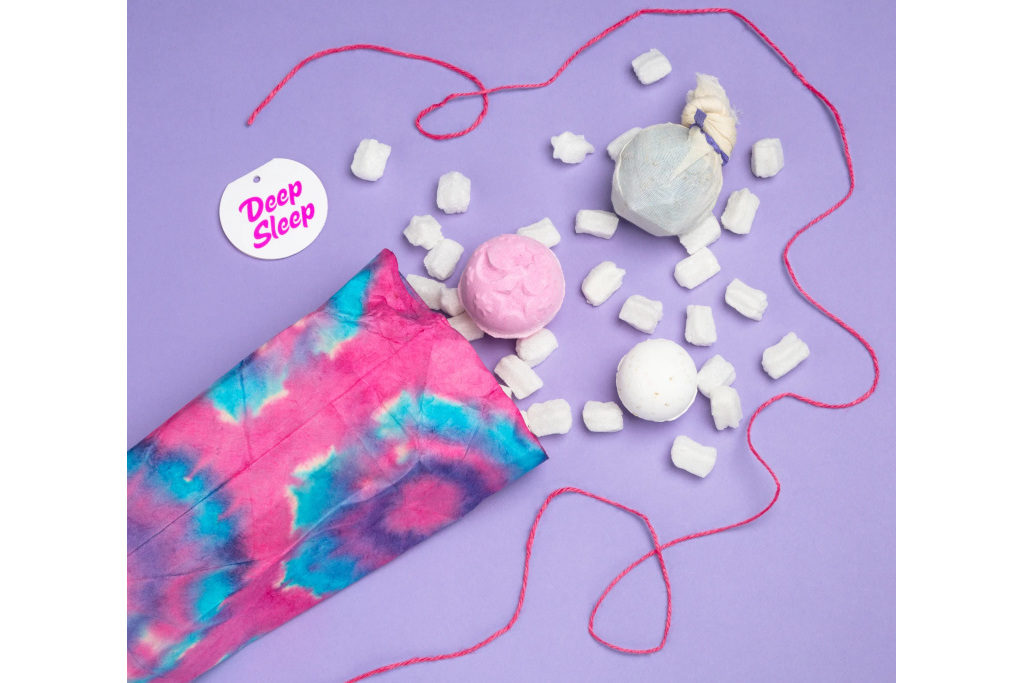 Pink package with bath bomb and pink string on purple background