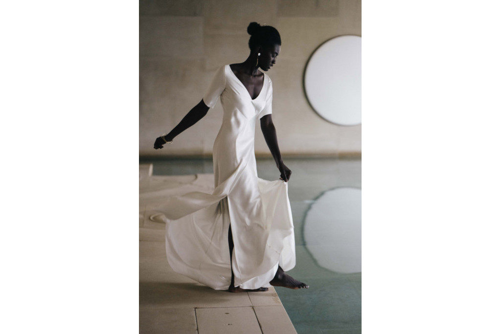 Model in wedding dress dipping her toe in an indoor pool