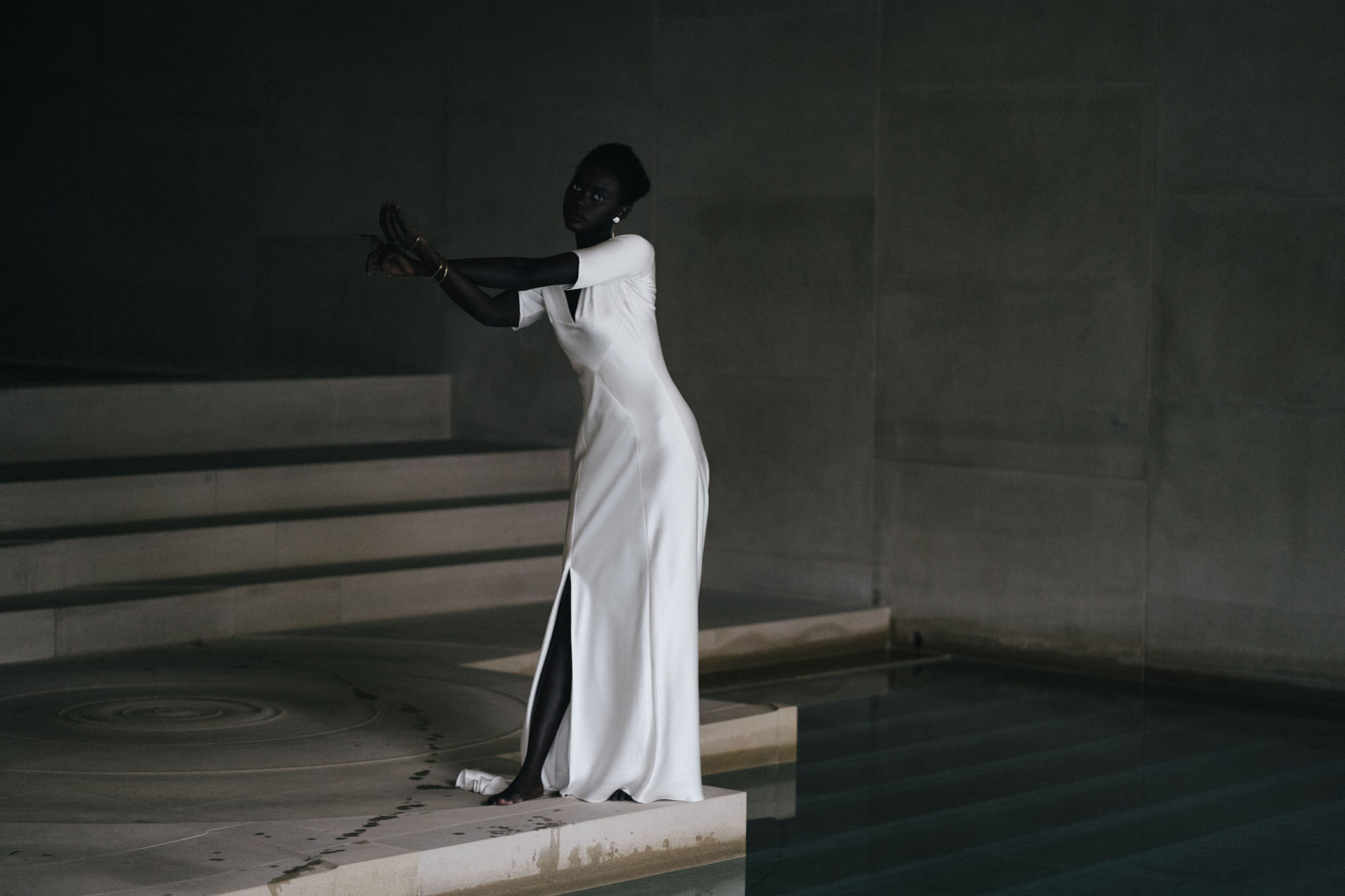 Model in a wedding dress strec=tching her arm by an indoor pool