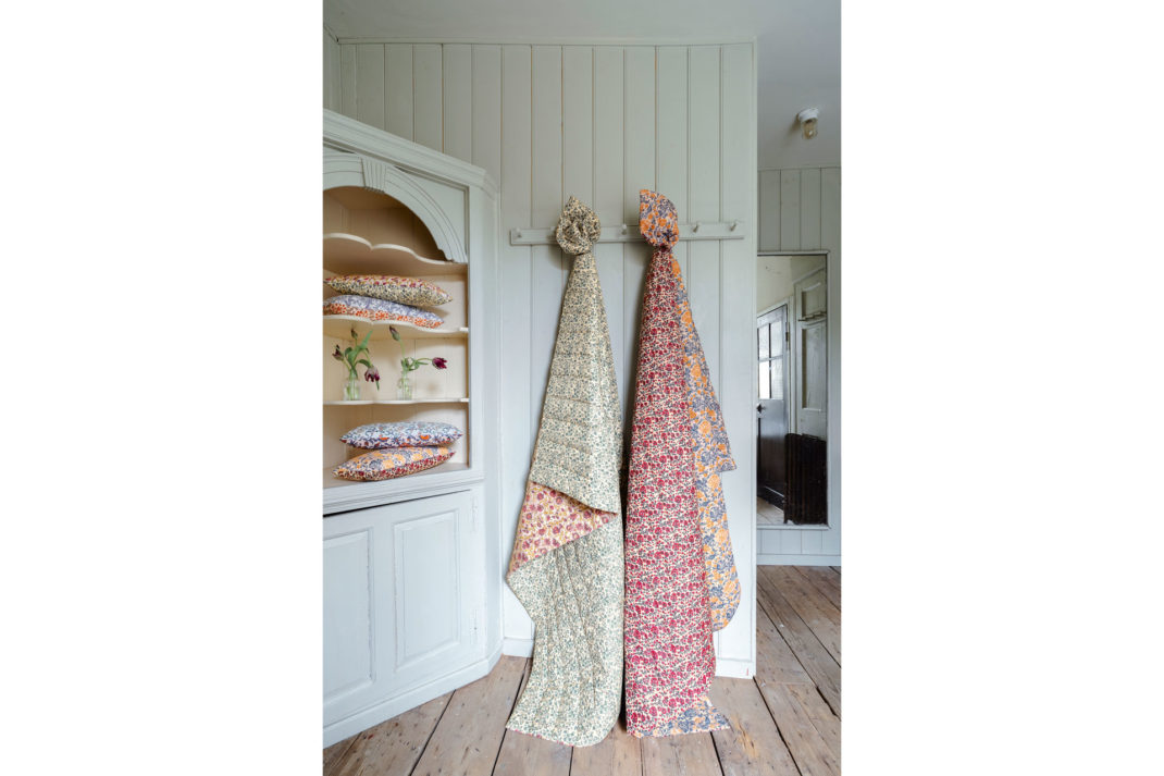 two chintzy quilts hung up in a light blue wood clad bedroom in a traditional English home