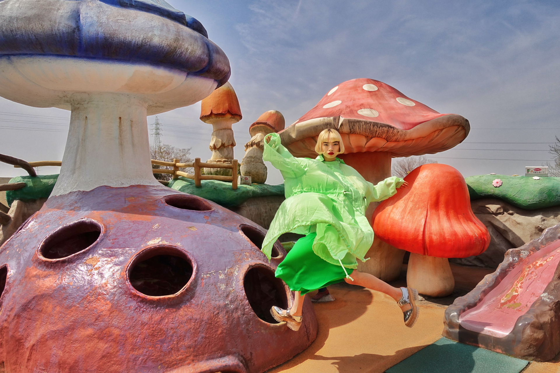 woman in green dress and overshirt jumping on mushroom sculptures